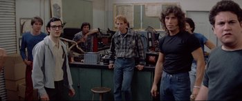 Movie still from “Christine” (1983), directed by John Carpenter – A group of men standing in a room next to each other; Medium shot, Over the shoulder angle