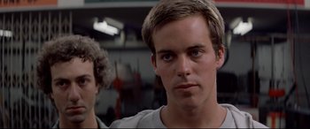 Movie still from “Christine” (1983), directed by John Carpenter – A young man with short blonde hair is looking at the camera; Close Up shot, Low angle