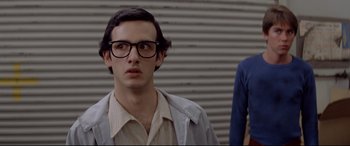 Movie still from “Christine” (1983), directed by John Carpenter – A young man wearing glasses standing in front of a wall; Close Up shot, Low angle