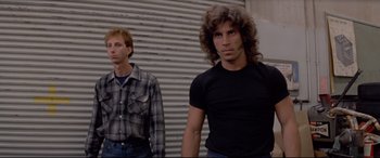 Movie still from “Christine” (1983), directed by John Carpenter – Two men standing next to each other in front of a wall; Medium shot, Low angle