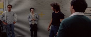 Movie still from “Christine” (1983), directed by John Carpenter – Two young men standing next to each other on a sidewalk; Medium shot, Over the shoulder angle