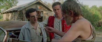 Movie still from “Christine” (1983), directed by John Carpenter – A group of men standing next to each other in front of a building; Medium shot, Over the shoulder angle