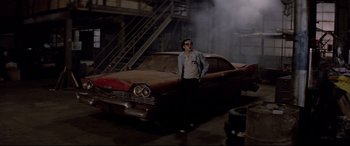 Movie still from “Christine” (1983), directed by John Carpenter – A man standing in front of an old red car; Wide shot, Low angle