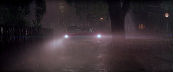 Movie still from “Christine” (1983), directed by John Carpenter – A car driving down a street in the rain; Extreme Wide shot, High angle