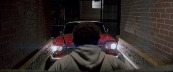 Movie still from “Christine” (1983), directed by John Carpenter – A man standing in front of a red classic car; Wide shot, Over the shoulder angle