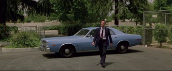 Movie still from “Christine” (1983), directed by John Carpenter – A man in a suit and tie walking past a blue car; Wide shot, Low angle
