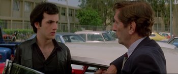Movie still from “Christine” (1983), directed by John Carpenter – Two men talking in front of a parked car in a parking lot; Close Up shot, Over the shoulder angle