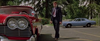 Movie still from “Christine” (1983), directed by John Carpenter – A man in a suit and tie standing next to a car; Medium shot, Low angle