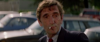 Movie still from “Christine” (1983), directed by John Carpenter – A person wearing a suit smoking a cigarette; Close Up shot, Low angle