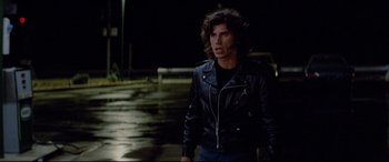 Movie still from “Christine” (1983), directed by John Carpenter – A man in a leather jacket walking down a street; Medium shot, Low angle