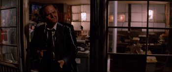 Movie still from “Christine” (1983), directed by John Carpenter – A man in a suit and tie standing next to a window; Medium shot, Over the shoulder angle