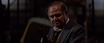 Movie still from “Christine” (1983), directed by John Carpenter – An older man in a suit and tie holding a guitar; Close Up shot, Low angle