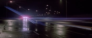 Movie still from “Christine” (1983), directed by John Carpenter – A night time photo of a street with lights on; Extreme Wide shot, Low angle