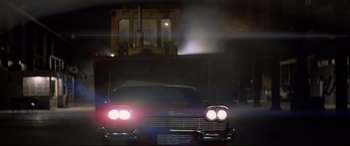 Movie still from “Christine” (1983), directed by John Carpenter – An old red car is driving down the street at night; Wide shot, Low angle