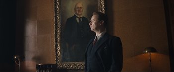Movie still from “Christopher Robin” (2018), directed by Marc Forster – A man standing in front of a painting of an older man; Medium shot, Low angle