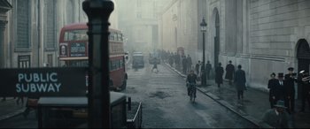 Movie still from “Christopher Robin” (2018), directed by Marc Forster – A man riding a bike down a street next to tall buildings; Extreme Wide shot, High angle