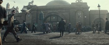 Movie still from “Christopher Robin” (2018), directed by Marc Forster – A group of people walking in front of a building; Extreme Wide shot, Low angle