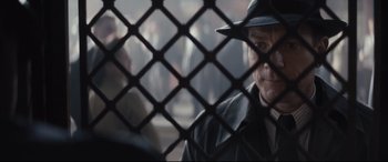 Movie still from “Christopher Robin” (2018), directed by Marc Forster – A man wearing a hat looking through a chain link fence; Close Up shot, Over the shoulder angle