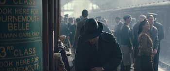 Movie still from “Christopher Robin” (2018), directed by Marc Forster – An old man in a hat and a black coat is in a train station; Medium shot, Over the shoulder angle