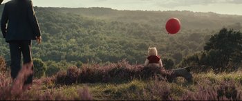 Movie still from “Christopher Robin” (2018), directed by Marc Forster – A white teddy bear sitting in a field with a red balloon; Extreme Wide shot, Low angle