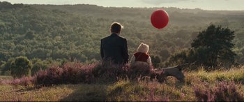 Movie still from “Christopher Robin” (2018), directed by Marc Forster – A man and a woman sitting in a field with a red balloon; Wide shot, High angle