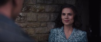 Movie still from “Christopher Robin” (2018), directed by Marc Forster – A woman is smiling in front of a stone wall; Close Up shot, Over the shoulder angle