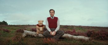 Movie still from “Christopher Robin” (2018), directed by Marc Forster – A man sitting on the ground next to a teddy bear; Medium shot, Low angle