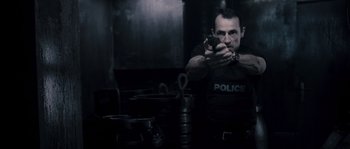 Movie still from “Chrysalis” (2007), directed by Julien Leclercq – A man in a police uniform holding a gun in a kitchen; Medium shot, Low angle