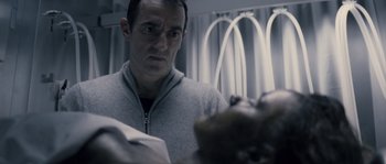 Movie still from “Chrysalis” (2007), directed by Julien Leclercq – A man standing next to a bed in a room; Close Up shot, Over the shoulder angle