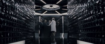 Movie still from “Chrysalis” (2007), directed by Julien Leclercq – A group of people standing around a table in a room; Wide shot, Overhead angle