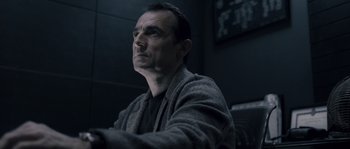 Movie still from “Chrysalis” (2007), directed by Julien Leclercq – A man sitting in front of a wall looking off to his right; Close Up shot, Low angle