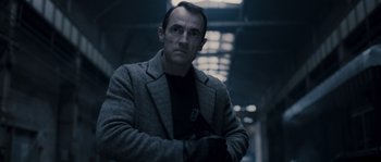 Movie still from “Chrysalis” (2007), directed by Julien Leclercq – A man in a gray coat and black shirt; Medium shot, Low angle