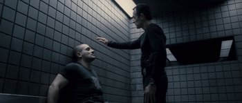 Movie still from “Chrysalis” (2007), directed by Julien Leclercq – Two men in black shirts one of which is sitting on the ground; Medium shot, Over the shoulder angle