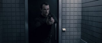 Movie still from “Chrysalis” (2007), directed by Julien Leclercq – A man holding a gun while standing next to a door; Medium shot, Low angle