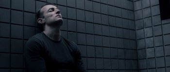 Movie still from “Chrysalis” (2007), directed by Julien Leclercq – A man in black shirt sitting in front of a wall; Close Up shot, Low angle