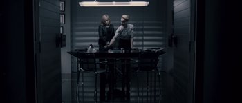 Movie still from “Chrysalis” (2007), directed by Julien Leclercq – Two women standing at a table in front of a wall; Wide shot, High angle