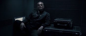 Movie still from “Chrysalis” (2007), directed by Julien Leclercq – A man sitting on a chair next to two suitcases; Medium shot, Low angle