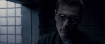 Movie still from “Chrysalis” (2007), directed by Julien Leclercq – A person wearing glasses and a jacket; Close Up shot, Low angle