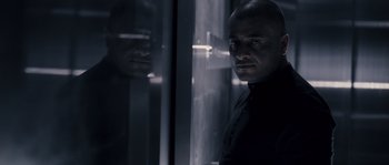 Movie still from “Chrysalis” (2007), directed by Julien Leclercq – A man standing in front of a glass window; Close Up shot, Low angle