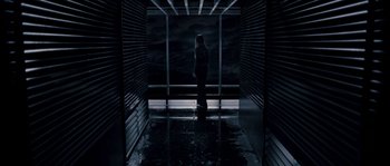 Movie still from “Chrysalis” (2007), directed by Julien Leclercq – A woman standing in front of a window in a dark room; Wide shot, High angle