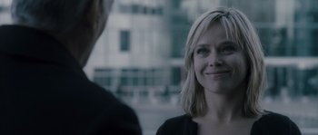Movie still from “Chrysalis” (2007), directed by Julien Leclercq – A woman smiles at the camera in front of a building; Close Up shot, Over the shoulder angle