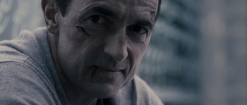 Movie still from “Chrysalis” (2007), directed by Julien Leclercq – An older man looking at the camera while wearing glasses; Close Up shot, Over the shoulder angle
