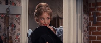 Movie still from “Cimarron” (1960), directed by Charles Walters – A young woman holding a black hat in a room; Close Up shot, Over the shoulder angle