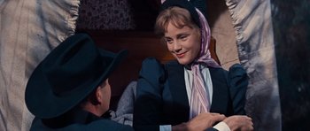 Movie still from “Cimarron” (1960), directed by Charles Walters – A woman in a hat and a scarf sitting next to a man in a suit; Medium shot, Over the shoulder angle