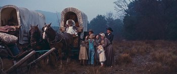 Movie still from “Cimarron” (1960), directed by Charles Walters – A group of people standing in front of a covered wagon on a field; Wide shot, Low angle