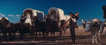 Movie still from “Cimarron” (1960), directed by Charles Walters – A group of people riding on the back of a covered wagon; Wide shot, Low angle
