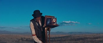 Movie still from “Cimarron” (1960), directed by Charles Walters – A man standing in the middle of a field with a camera; Medium shot, Low angle