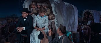 Movie still from “Cimarron” (1960), directed by Charles Walters – A man and a group of children sitting in front of a tent; Medium shot, High angle