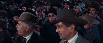 Movie still from “Cimarron” (1960), directed by Charles Walters – A group of men in suits and hats are gathered together; Medium shot, Over the shoulder angle