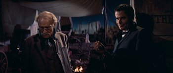 Movie still from “Cimarron” (1960), directed by Charles Walters – Two men standing next to each other near a fire pit; Medium shot, Over the shoulder angle